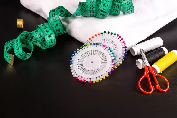 White fabric with needles, threads, measuring tape and scissors on black background