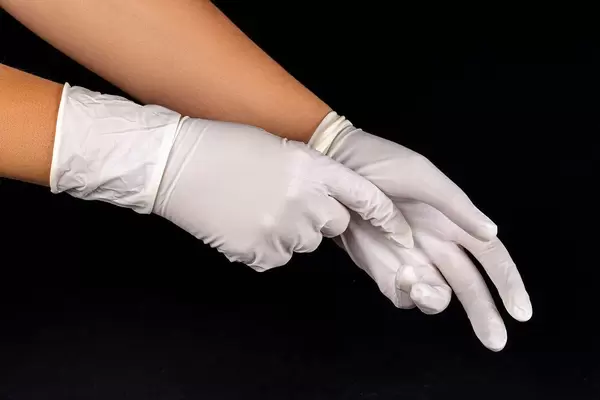 White latex medical gloves on a woman's hands on dark background