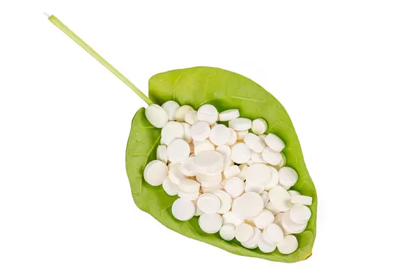 White pills lying on a green leaf, white background