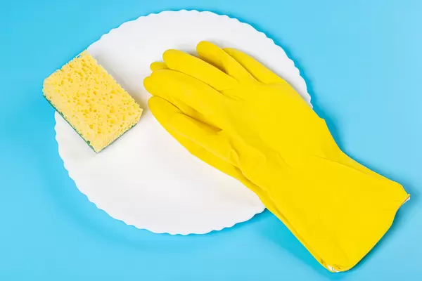 White plate, rubber gloves and a sponge on a blue background