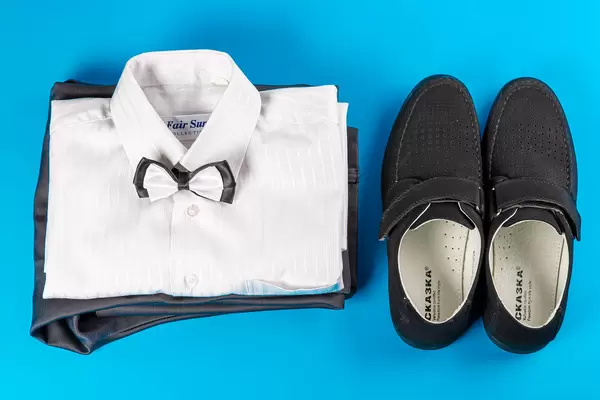 White shirt, trousers and black shoes on a blue background, children's clothing