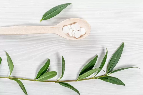 White-tablets-in-a-wooden-spoon-and-a-branch-with-green-leaves-on-a-white-wooden-background.jpg