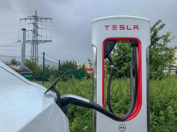 White Tesla Model 3 refuels at a Supercharger - charging station in rainy weather