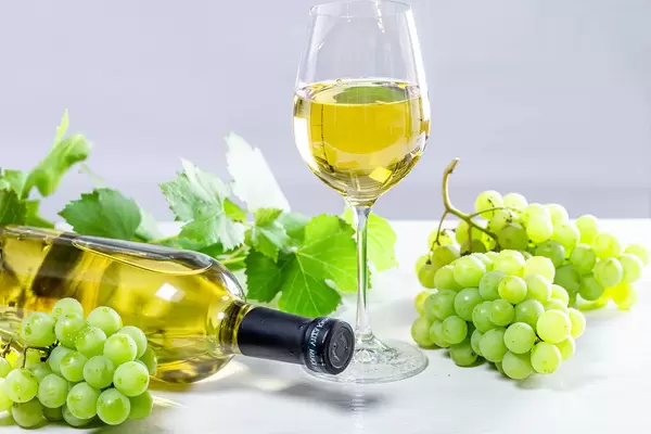 White wine in a glass with a full bottle, grapes and leaves on a white wooden background (Flip 2019)