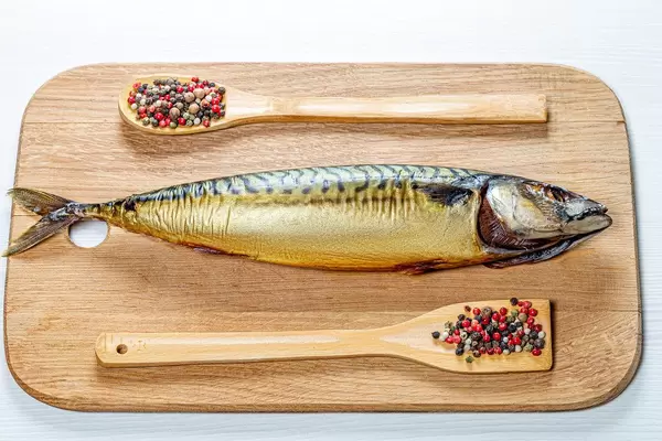 Whole smoked mackerel on a wooden kitchen Board with a mix of peppers. Top view (Flip 2019)