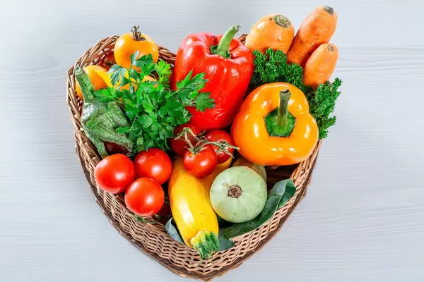 Wicker basket in the shape of a heart filled with fresh vegetables and herbs