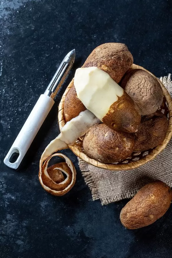 Wicker basket with raw potatoes on burlap and potato peeler