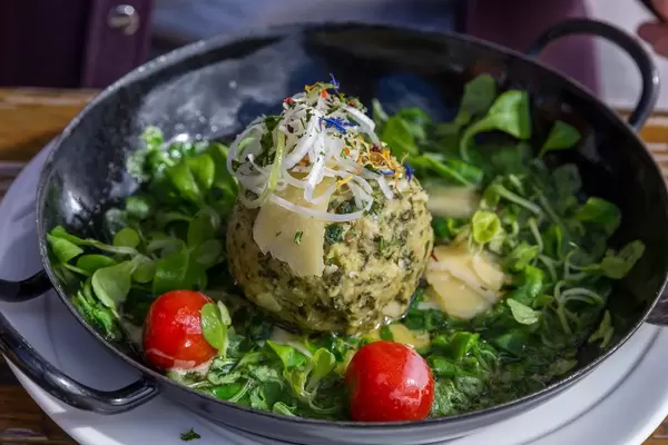 Wild garlic Knödel (Alpine dumpling) in a pan with salad and tomatoes at Dauerstoa Alm in Alpbach