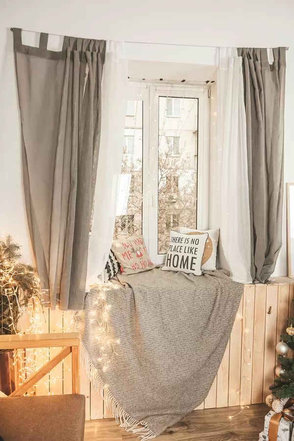 Window with garlands, pillows and a plaid on the windowsill, the concept of home decoration for the winter holidays