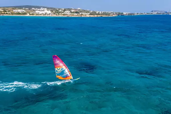 Windsurfer auf einem Surfbrett mit buntem Segel auf dem klaren Meer vor Paros, Griechenland