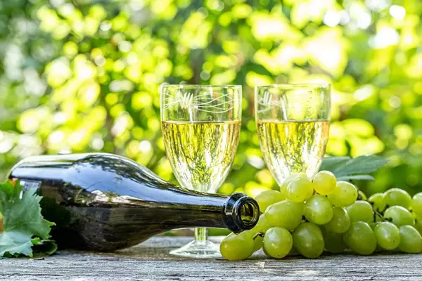Wine in glasses with a bottle and fresh grapes on a blurred bokeh background of nature