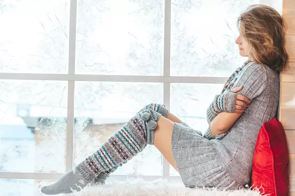Winter background, girl sitting by the window with a frosty pattern