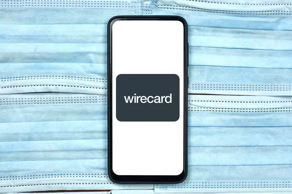 Wirecard logo on smartphone screen over the face masks. Global company during coronavirus crisis