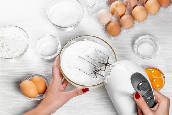 Woman beats egg whites with a mixer. Top view of the process of making a pie