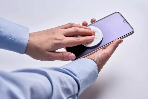 Woman cleaning display of smart phone with antibacterial white tissue or disposable wipe