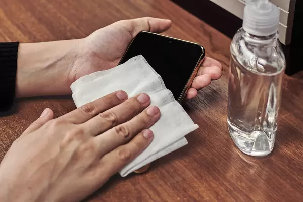 Woman cleaning smartphone with wet wipe at wooden table