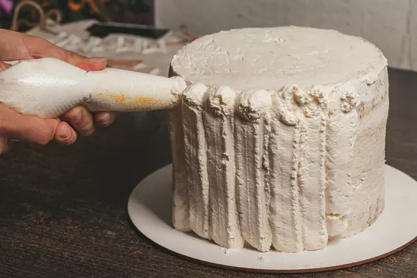 Woman covering cake with cream using pastry bag