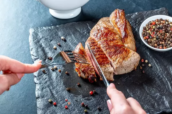 Woman cuts fresh steak with a knife and fork