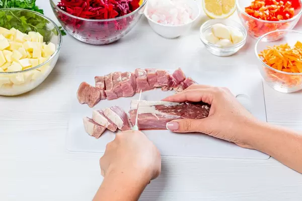 Woman cuts pork meat on white wooden table (Flip 2019)