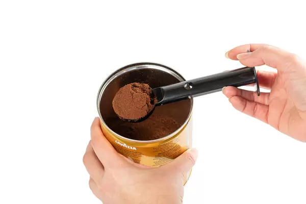 Woman dials ground coffee into a measuring spoon