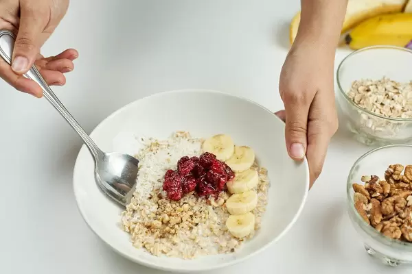 Woman eating healthy breakfast with oats, raspberries and banana slices