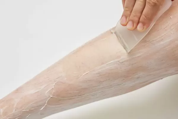 Woman epilating legs depilatory cream and remove it with a spatula