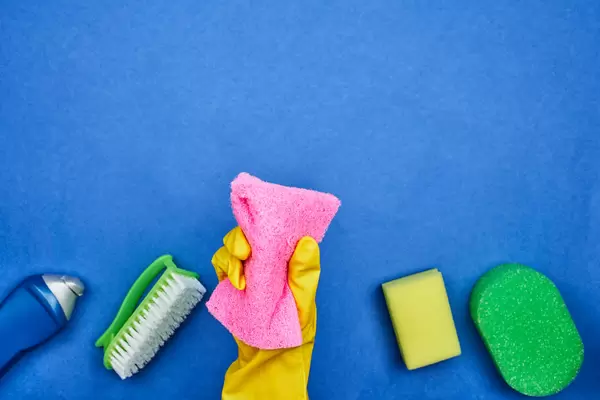 Woman hand with rubber gloves holds a sponge over blue background