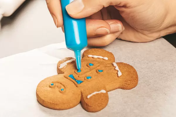 Woman hands decorating homemade gingerbread cookies with icing, close up. Festive culinary and new year traditions concept