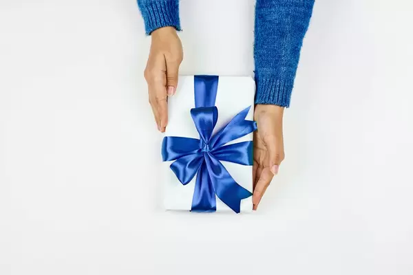 Woman hands in a blue sweater holding a gift box tied with a blue ribbon