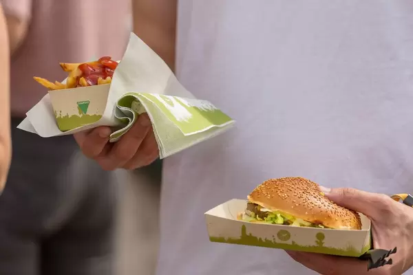 Woman has a hamburger and french fries with ketchup on compostable paperplates in her hands at the Tomorrowland festival in Belgium
