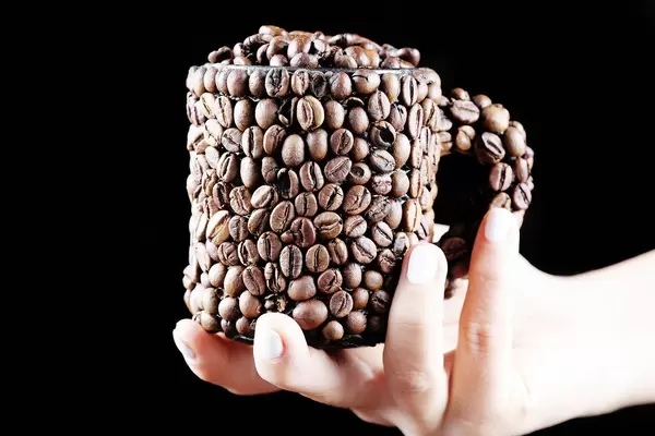 Woman holding a cup of coffee beans in her hand, black background