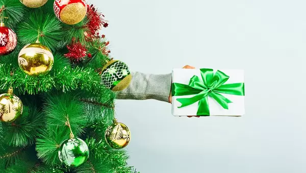Woman holding a gift box over the decorated with festive ornaments Christmas tree