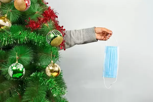 Woman holding a medical face mask over the decorated Xmas tree