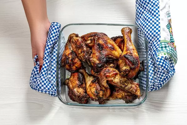 Woman holds potholders glass baking tray with baked chicken pieces (Flip 2019)