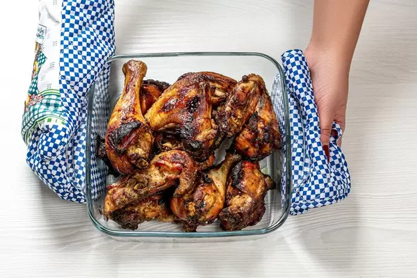Woman holds potholders glass baking tray with baked chicken pieces