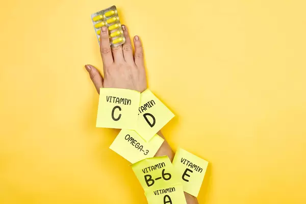 Woman holds vitamin pills on yellow