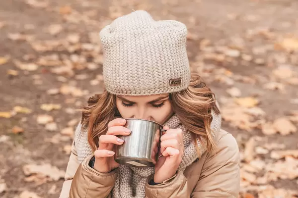Woman in autumn park drinking tea from an iron mug
