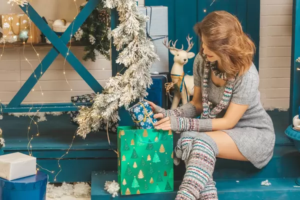 Woman in gray knitted dress with a scarf puts a present in a gift bag