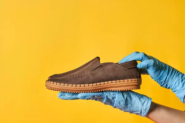 Woman in medical gloves holds a trendy leather shoe