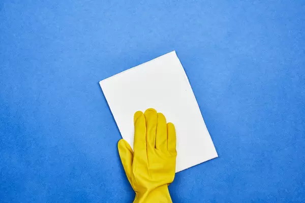 Woman in rubber gloves cleaning blue surface with a wipe