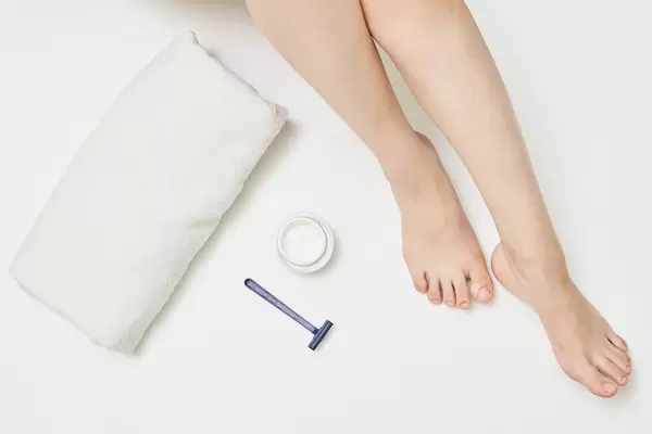 Woman leg, towel, razor and cosmetic cream on white background