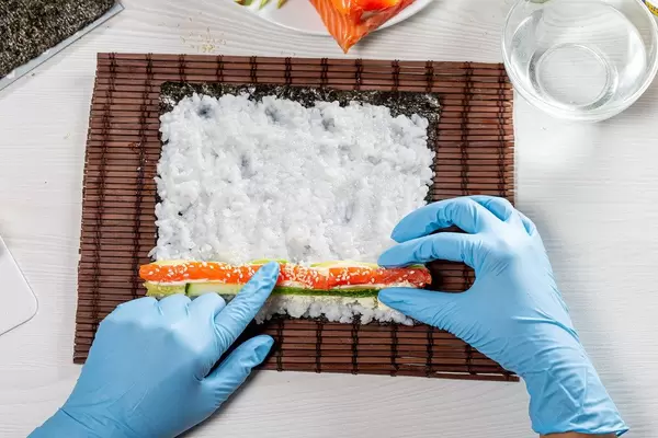 Woman making a maki roll with seaweed and japanese rice on Sushi Roll mat (Flip 2019)