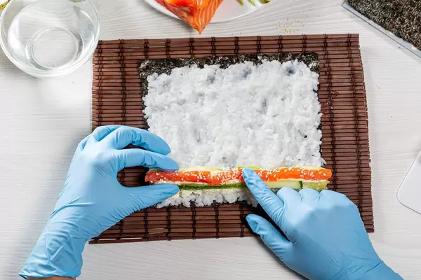 Woman making a maki roll with seaweed and japanese rice on Sushi Roll mat