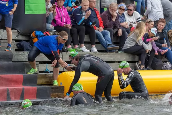 Woman of the Ironman team helps swimmer to climb out of the lake after the first triathlon stage