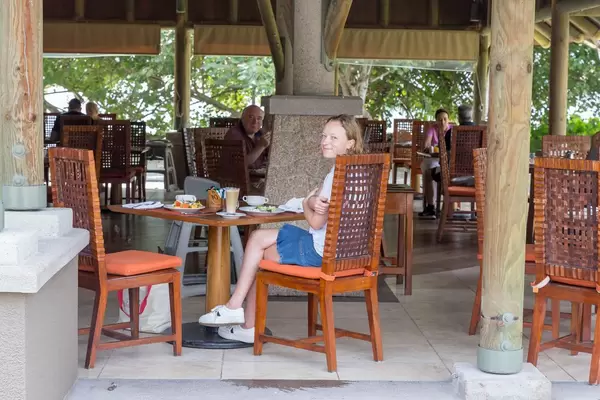 Woman on vacation with cappuccino on wooden rattan chair in cafe of Constance Ephelia Resort in Mahé, Seychelles Island