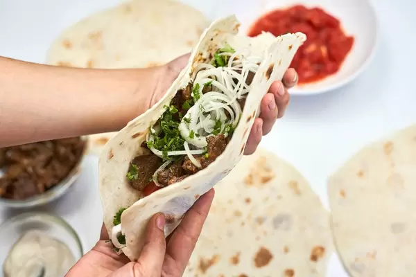 Woman preparing shawarma sandwich - roll of lavash filled with grilled meat, onions and sauce