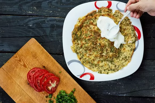 Woman putting fresh sour cream on the green herb based omelet