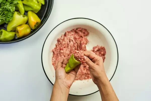 Woman putting minced meat into the green bell pepper