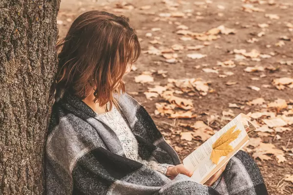 Woman sitting in the forest and reading a book, autumn rest