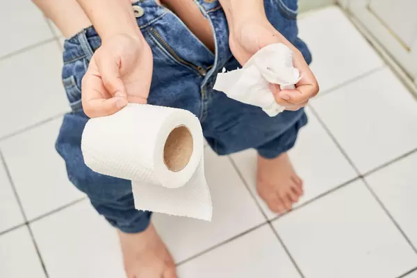 Woman sitting on toilet with toilet paper - constipation concept